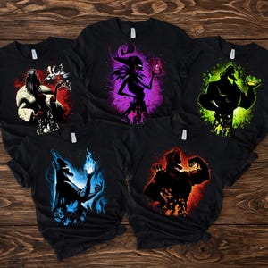 May include: Five black t-shirts with colorful graphic designs. Each shirt features a different character silhouette with vibrant color accents: red, purple, green, blue, and orange. The designs are set against a dark background.