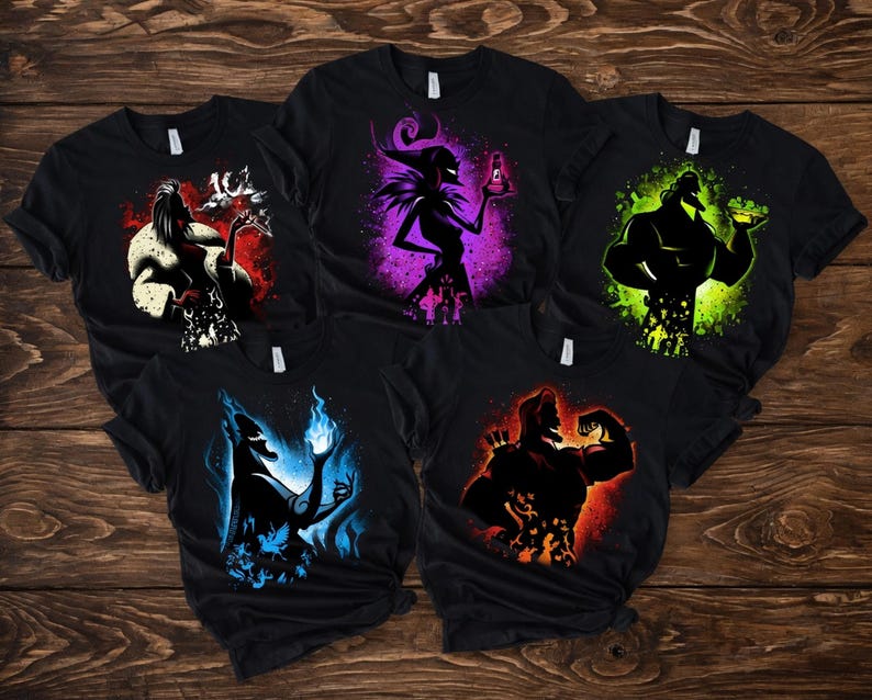 May include: Five black t-shirts with colorful graphic designs. Each shirt features a different character silhouette with vibrant color accents: red, purple, green, blue, and orange. The designs are set against a dark background.