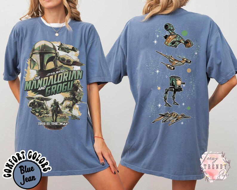 Pode incluir: Uma t-shirt azul de manga curta com uma impress&atilde;o gr&aacute;fica de The Mandalorian e Grogu na frente, com o texto "The Mandalorian and Grogu" e "This is the way". As costas exibem um alinhamento vertical de quatro naves espaciais.