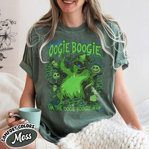 Op de afbeelding: Groen t-shirt met een afbeelding van Oogie Boogie uit The Nightmare Before Christmas. Het ontwerp bevat de tekst "Oogie Boogie" en "I'm the Oogie Boogie Man!" in een distressed stijl. Het shirt is in de kleur Comfort Colors Moss.
