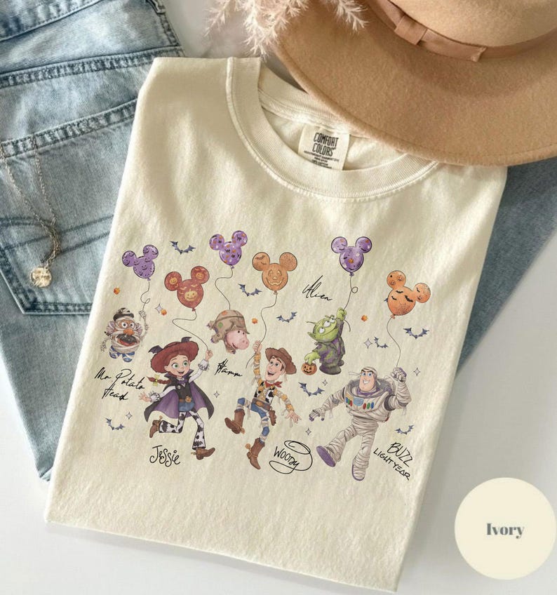 May include: Ivory-colored crew neck sweatshirt featuring a colorful graphic of Disney characters holding Mickey Mouse-shaped balloons. The design includes characters like Woody, Buzz Lightyear, and Jessie. The sweatshirt is made of a soft material.