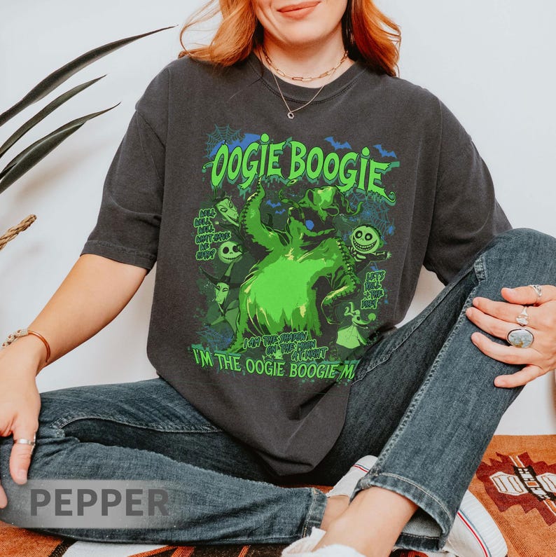 Op de afbeelding: Donkergrijs T-shirt met een neon groen Oogie Boogie-ontwerp uit The Nightmare Before Christmas. Het ontwerp bevat de tekst "Oogie Boogie" en "I'm the Oogie Boogie Man". Het shirt heeft een relaxte pasvorm.