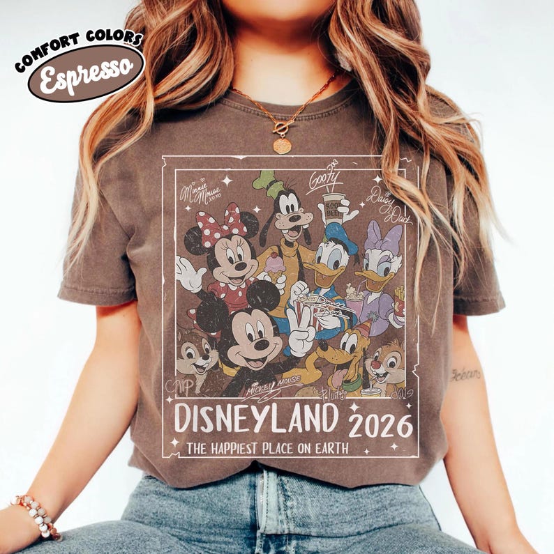 May include: Espresso-coloured t-shirt with a vintage Disneyland 2026 graphic. The design features Mickey Mouse, Minnie Mouse, Goofy, Donald Duck, Daisy Duck, and Chip and Dale. The text reads "The Happiest Place on Earth."