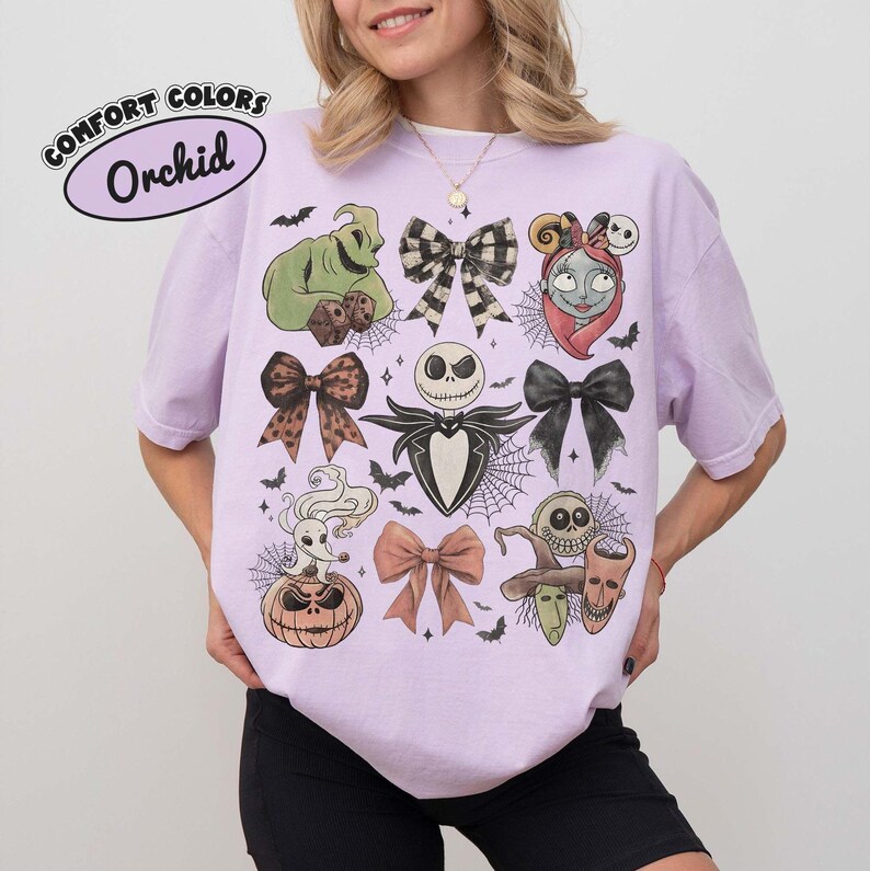 May include: An orchid-colored t-shirt featuring a graphic print of characters from The Nightmare Before Christmas, including Jack Skellington, Sally, Zero, and Oogie Boogie, interspersed with various bows, spiderwebs, and small bats.