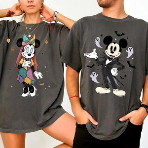 May include: Two dark gray t-shirts featuring Disney characters. One shirt displays Minnie Mouse in a patchwork dress, the other shows Mickey Mouse dressed as Jack Skellington, surrounded by bats and ghosts. Both shirts have a vintage, faded look.