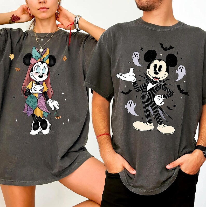 May include: Two dark gray t-shirts featuring Disney characters. One shirt displays Minnie Mouse in a patchwork dress, the other shows Mickey Mouse dressed as Jack Skellington, surrounded by bats and ghosts. Both shirts have a vintage, faded look.