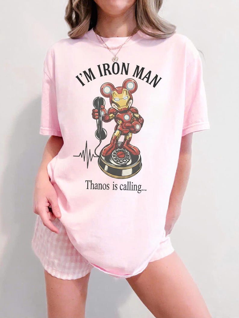 Op de afbeelding: Lichtroze T-shirt met de tekst "I'M IRON MAN" boven een cartoonillustratie van Iron Man als Mickey Mouse op een draaitelefoon. De tekst "Thanos is calling..." staat eronder.