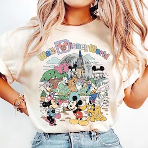 May include: Cream-colored t-shirt featuring a colorful graphic of Disney characters, including Mickey Mouse, Minnie Mouse, Donald Duck, and Goofy, in front of a castle and the words "Walt Disney World".