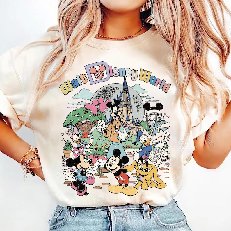 May include: Cream-colored t-shirt featuring a colorful graphic of Disney characters, including Mickey Mouse, Minnie Mouse, Donald Duck, and Goofy, in front of a castle and the words "Walt Disney World".