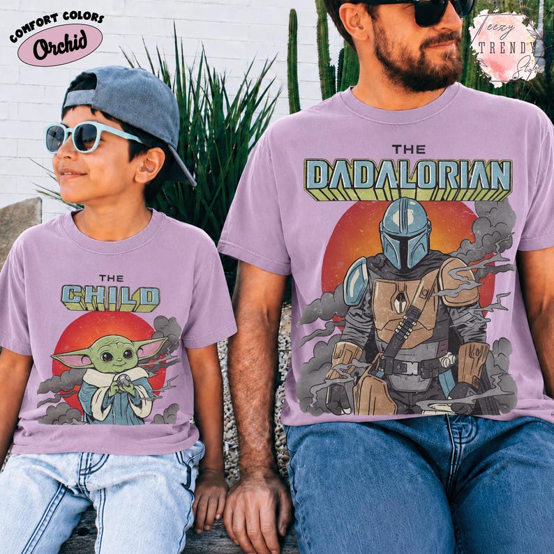 May include: Two light purple t-shirts featuring graphic prints. The smaller shirt displays a green character with the text THE CHILD above a red sun. The larger shirt shows a armored character with the text THE DADALORIAN above a red sun.