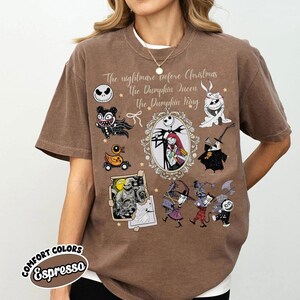 Pu&ograve; includere: T-shirt marrone con personaggi e testo da "Nightmare Before Christmas". Il design include Jack Skellington, Sally e altri personaggi. La maglietta ha il testo "The Nightmare Before Christmas, The Pumpkin Queen, The Pumpkin King."