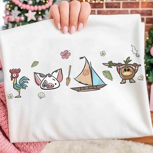 Pode incluir: Uma t-shirt branca com uma estampa gr&aacute;fica de um galo de desenho animado, um leit&atilde;o, um remo de madeira, um veleiro com uma vela em espiral e uma pequena criatura de coco segurando uma lan&ccedil;a, decorada com flores e conchas tropicais.