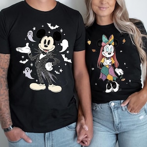 May include: Black t-shirts featuring Disney characters in Halloween costumes. One shirt has Mickey Mouse dressed as Jack Skellington, surrounded by bats and ghosts. The other shirt has Minnie Mouse in a patchwork costume with autumn leaves.