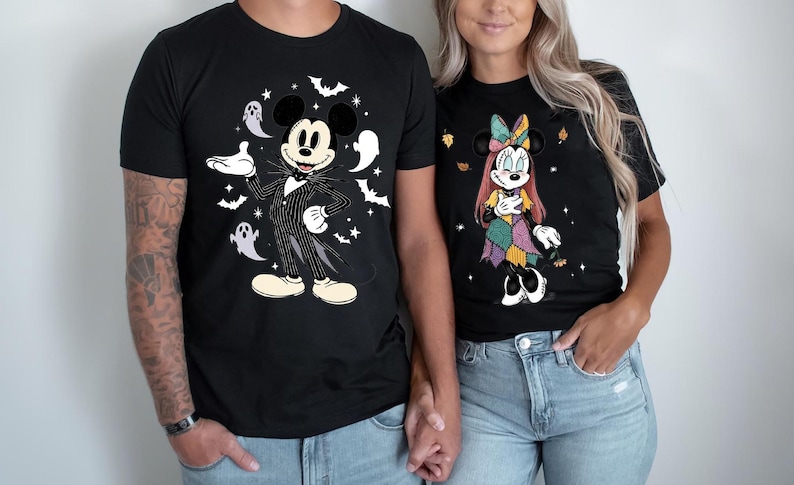 May include: Black t-shirts featuring Disney characters in Halloween costumes. One shirt has Mickey Mouse dressed as Jack Skellington, surrounded by bats and ghosts. The other shirt has Minnie Mouse in a patchwork costume with autumn leaves.