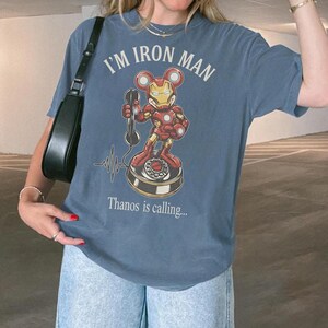 Op de afbeelding: Blauw T-shirt met de tekst "I'M IRON MAN" en een cartoonafbeelding van Iron Man als Mickey Mouse die een telefoon vasthoudt. De tekst "Thanos is calling..." staat eronder.