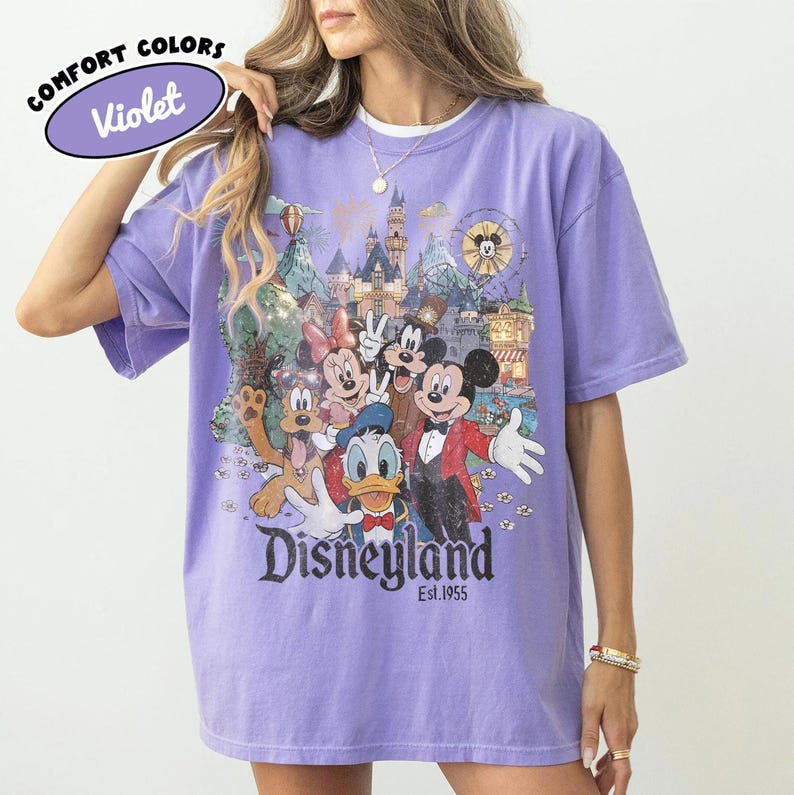 May include: Violet Comfort Colors t-shirt featuring a Disneyland graphic with Mickey Mouse, Minnie Mouse, Donald Duck, Goofy, and other characters. The shirt has a vintage-style design with the text "Disneyland Est.1955".