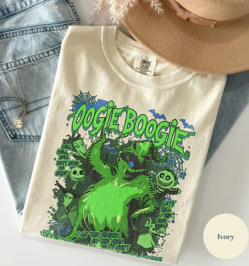 Op de afbeelding: Ivoor kleurig T-shirt met een groene afbeelding van Oogie Boogie uit The Nightmare Before Christmas. Het ontwerp bevat de tekst "Oogie Boogie" en "I am the shadow on the moon at night."