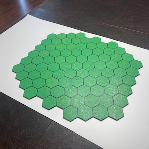 May include: A collection of green hexagonal tiles arranged in a large, irregular shape. The tiles are a vibrant green color with a textured surface, and are set against a white background. The tiles appear to be made of a durable material.