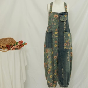 May include: Denim dungarees with a floral print panel and a denim panel. The overalls have a loose fit, pockets and adjustable straps. A woven bag and flowers are on a table.