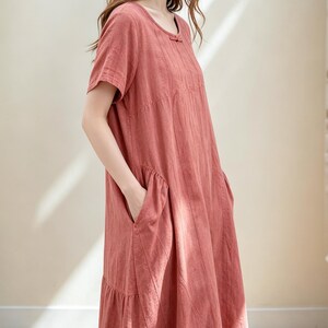Può includere: Abito in lino color rosa antico con maniche corte e scollo tondo. L'abito presenta dettagli di cucitura verticali, un piccolo fiocco sullo scollo e due ampie tasche. L'abito ha una gonna a balze e arriva al ginocchio.