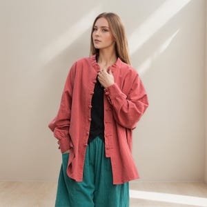 Puede incluir: Una camisa de manga larga de color coral con cuello mandarín y cierres de botón. La camisa se combina con una parte superior negra y pantalones de color turquesa. Las mangas tienen puños abotonados. El atuendo es informal y cómodo.