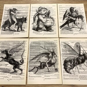 以下が含まれることがあります： 6つのアンティーク辞書ページ。白黒のイラストで空想上の生き物が描かれています。翼のある犬、王笏を持ったカラス、象の頭を持つ生き物などが含まれています。