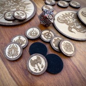 May include: A set of wooden game pieces featuring various symbols, such as a sword, a gear, a flame, and a crescent moon. The pieces are laid out on a wooden surface alongside a black and white dice and a wooden board with a skull design.
