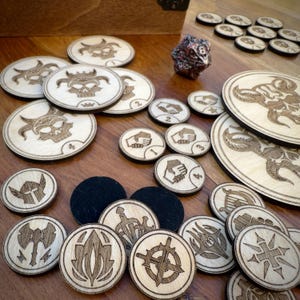 May include: A set of wooden game pieces featuring various symbols, including skulls, swords, and hands. The pieces are laid out on a wooden table with a black and white dice in the background.