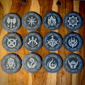 May include: A set of twelve circular slate coasters, each featuring a unique engraved symbol representing a character class. The designs include icons for Barbarian, Cleric, Druid, Artificer, Fighter, Ranger, Rogue, Warlock, Monk, Wizard, Sorcerer, and Paladin.