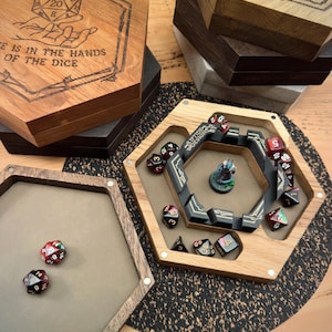 May include: A set of hexagonal wooden dice boxes with lids featuring laser-engraved designs and text including "THE IS IN THE HANDS OF THE DICE" and "ROLL FOR INITIATIVE". One open box contains a miniature figure and multiple polyhedral dice.
