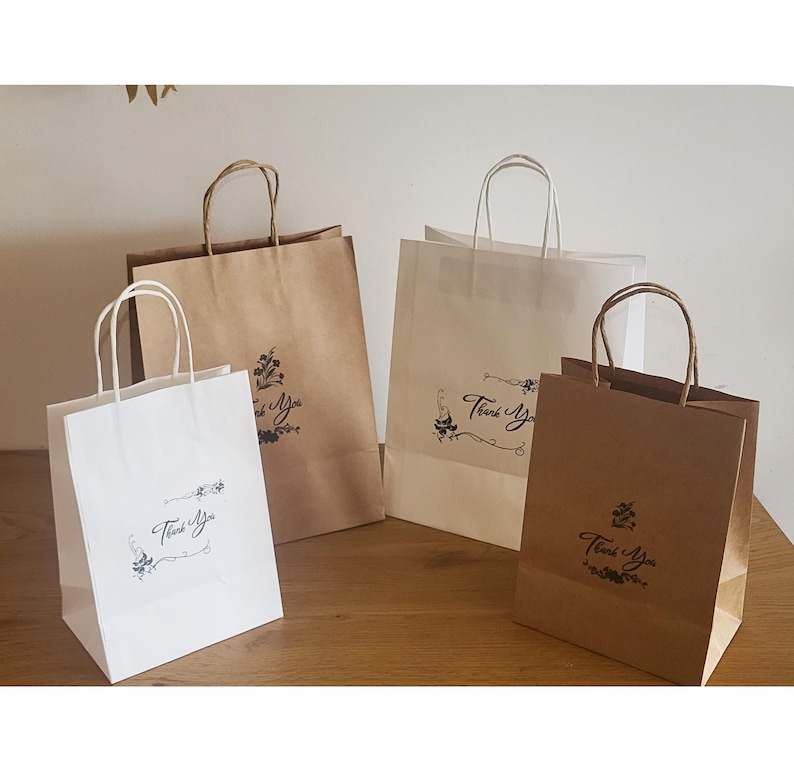 May include: Four paper gift bags with handles. Two bags are brown with a black "Thank You" design and two bags are white with a black "Thank You" design.