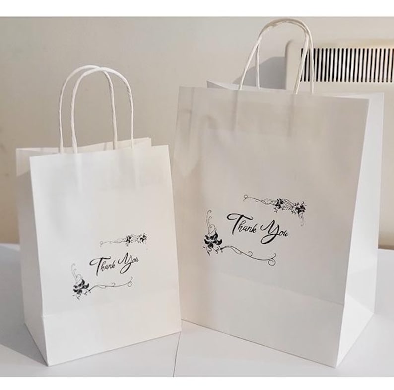 May include: Two white paper gift bags with black handles and floral designs. The larger bag has the text "Thank You" printed on it.