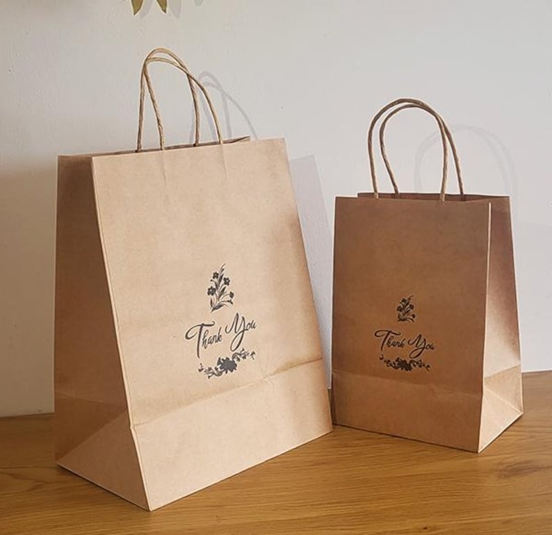 May include: Two brown paper gift bags with handles. Both bags have a floral design and the text "Thank You" printed on them.