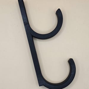 Könnte beinhalten: Schwarzer Doppelhaken aus Kunststoff für die Wandmontage. Der Haken ist so konzipiert, dass er Gegenstände wie Handtücher, Bademäntel oder Taschen hält.