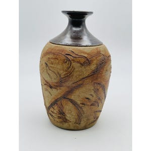 Könnte beinhalten: Eine braune Keramikvase mit einem dunkelbraunen Überzug am oberen Rand und einem strukturierten Design aus wirbelnden Linien und Formen.