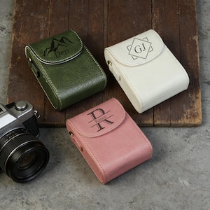 Può includere: Tre custodie in pelle personalizzate in verde, bianco e rosa. La custodia verde ha una grafica di montagna e il nome "Den". La custodia bianca ha le iniziali "GJ". La custodia rosa ha l'iniziale "R" e il nome "Rance".