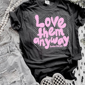 May include: Black t-shirt with a pink graphic that says "Love them anyway" with the Bible verse "Luke 23:34" underneath.