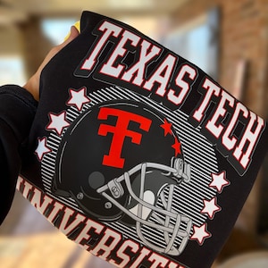 May include: Black sweatshirt featuring the words "TEXAS TECH UNIVERSITY" in white with a red outline. A black football helmet with a red "T" is in the center, surrounded by white stars. The sweatshirt is held up.