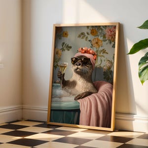 May include: Framed art print featuring an otter in a bathtub, wearing sunglasses and a pink turban with flowers. The otter holds a glass of champagne. The background has a floral wallpaper design. The print is in a wooden frame.