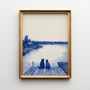Könnte beinhalten: Gerahmter Kunstdruck mit einer blau-weißen Illustration von zwei Katzen auf einem Holzsteg mit Blick auf einen See. Das Kunstwerk hat eine Vintage-Ästhetik mit einem goldenen Rahmen.