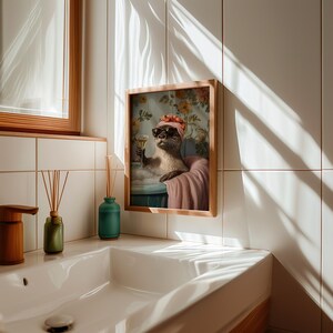 May include: A framed print featuring an otter in a bathtub, wearing sunglasses and a headscarf, holding a champagne glass. The artwork has a vintage style with floral wallpaper in the background. The frame is made of light-colored wood.