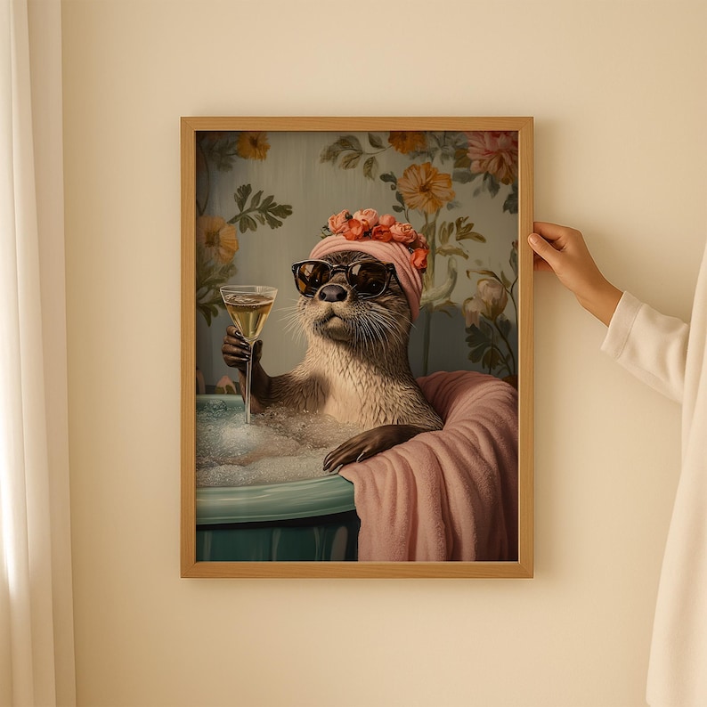 May include: A framed art print featuring an otter in a bathtub, wearing sunglasses and a floral head wrap, holding a glass of champagne. The otter is surrounded by bubbles and a pink towel, with a floral wallpaper background.