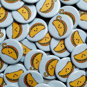 Puede incluir: Una colecci&oacute;n de botones redondos de color azul claro con un contorno blanco. Cada bot&oacute;n presenta un gato de dibujos animados con un disfraz de taco. Los gatos est&aacute;n en varias poses, algunos est&aacute;n sentados, otros est&aacute;n de pie y otros est&aacute;n acostados. Los tacos est&aacute;n rellenos de diferentes ingredientes, como queso, lechuga y tomates.