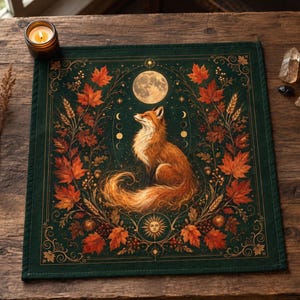 May include: A square dark green fabric altar cloth featuring a central illustration of a red fox surrounded by a wreath of orange and red autumn maple leaves, wheat stalks, a full moon, and a sun symbol with celestial moon phase icons.
