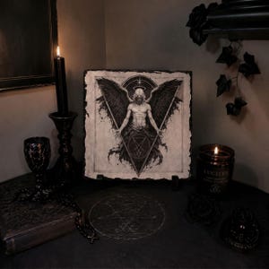 Puede incluir: Ilustraci&oacute;n en blanco y negro de un &aacute;ngel con grandes alas y un halo, dentro de un tri&aacute;ngulo. La obra de arte est&aacute; sobre papel texturizado, expuesta sobre un soporte. Tambi&eacute;n se ven una vela negra encendida, una copa y una vela en tarro.