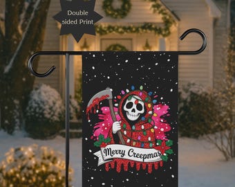 Puede incluir: Bandera de jardín negra con un diseño de la Parca, sosteniendo una guadaña y adornada con luces navideñas. La bandera tiene el texto "Merry Creepmas" en una pancarta. La bandera de doble cara se muestra al aire libre en un entorno nevado.