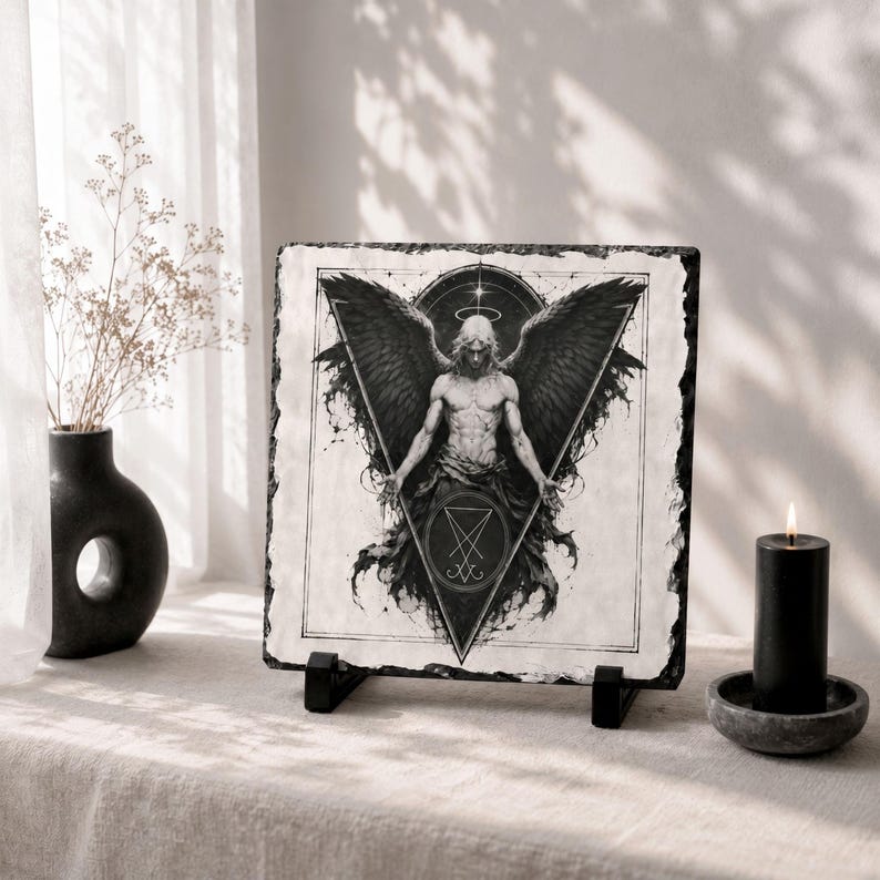 May include: A black and white illustration of an angel with large wings, a halo, and a triangle design. The artwork is displayed on a square slate tile, propped up on a black stand. A black candle and vase are also in the image.