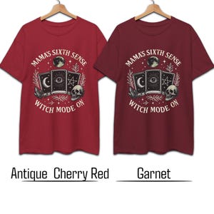 K&ouml;nnte beinhalten: Zwei rote T-Shirts mit einem grafischen Design mit Tarotkarten, einem Totenkopf und dem Text "MAMA'S SIXTH SENSE WITCH MODE ON." Die Shirts sind in Antik-Kirschrot und Granat gehalten.