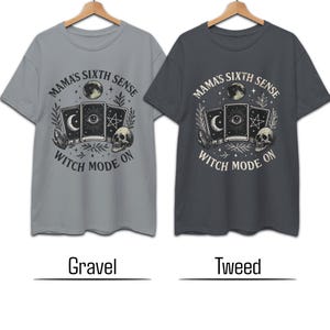 K&ouml;nnte beinhalten: Zwei kurz&auml;rmelige T-Shirts, eines grau und eines dunkelgrau, mit einem grafischen Design. Das Design zeigt Tarotkarten, einen Totenkopf, einen Mond und den Text "Mama's Sixth Sense Witch Mode On."
