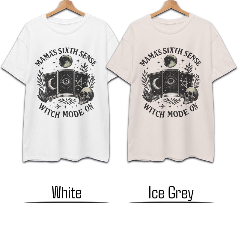 K&ouml;nnte beinhalten: Zwei T-Shirts, eines in Wei&szlig; und eines in Eisgrau, jeweils mit einem grafischen Design. Das Design enth&auml;lt den Text "MAMA'S SIXTH SENSE" &uuml;ber einer Tarotkarten-Illustration, einem Mond und einem Totenkopf. Der Text "WITCH MODE ON" steht darunter.
